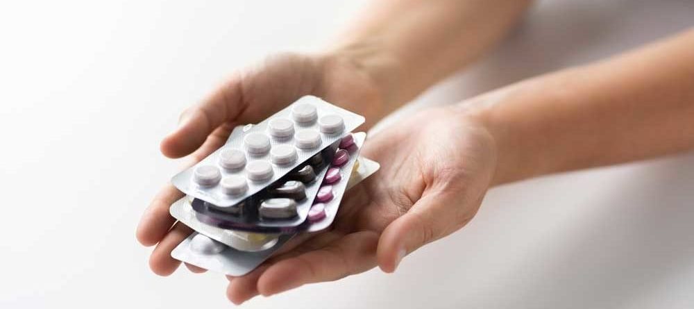 Hände halten mehrere Blisterverpackungen mit unterschiedlichen Tabletten in verschiedenen Farben.