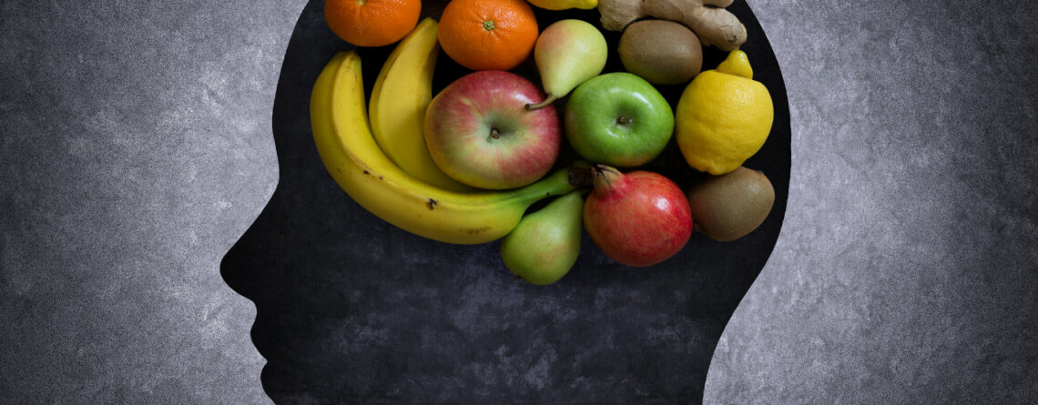 Silhouette eines Kopfes, gefüllt mit verschiedenen Früchten wie Äpfeln, Bananen, Orangen und Zitrusfrüchten auf dunklem Hintergrund.